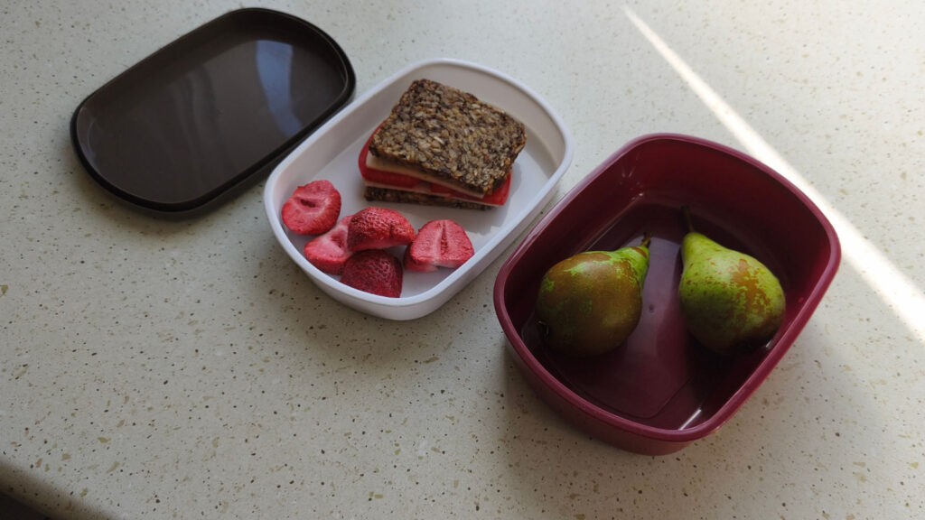 Otwarta śniadaniówka na stole z kanapką, gruszkami i liofilizowanymi truskawkami Kamifood